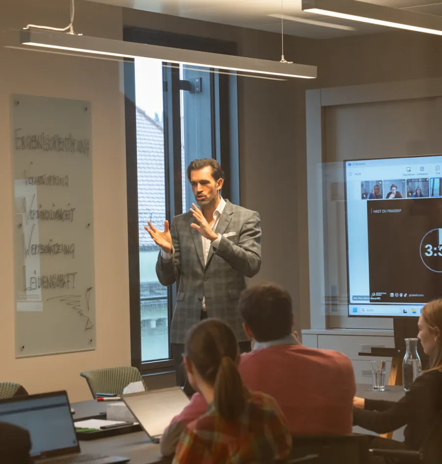 Alex Khan erklärt im KI-Workshop bei der Lenyx Group, durch die Glaswand des Besprechungsraums fotografiert