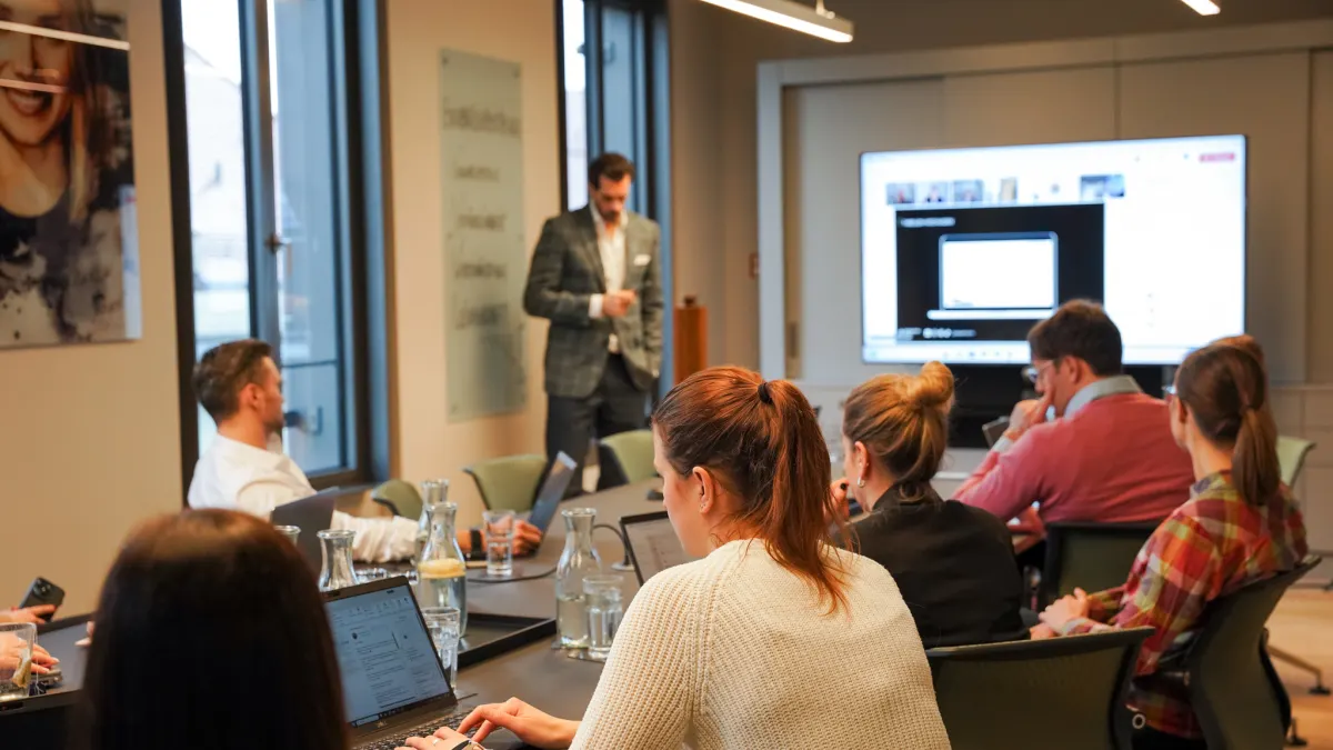 Teilnehmende eines KI-Workshops verfolgen eine Live-Demo von Alex Khan am großen Bildschirm