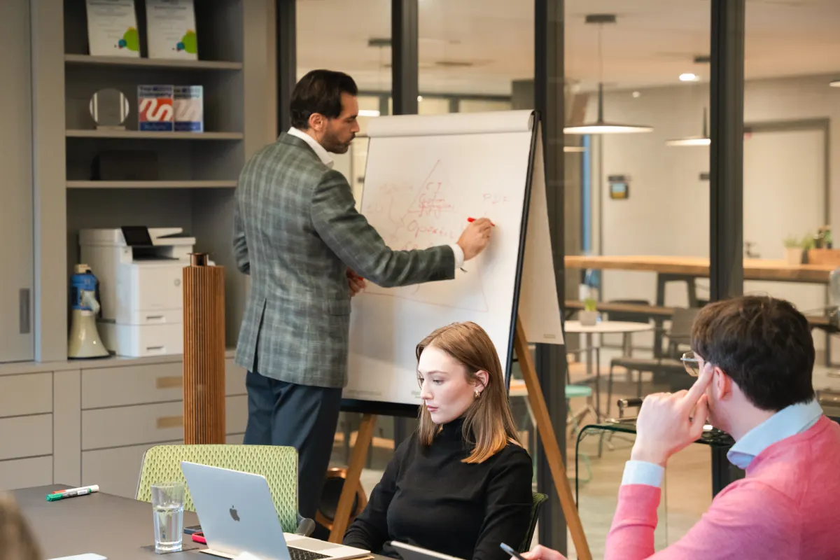 Alex Khan erklärt im KI-Workshop am Flipchart, zwei Teilnehmende hören zu
