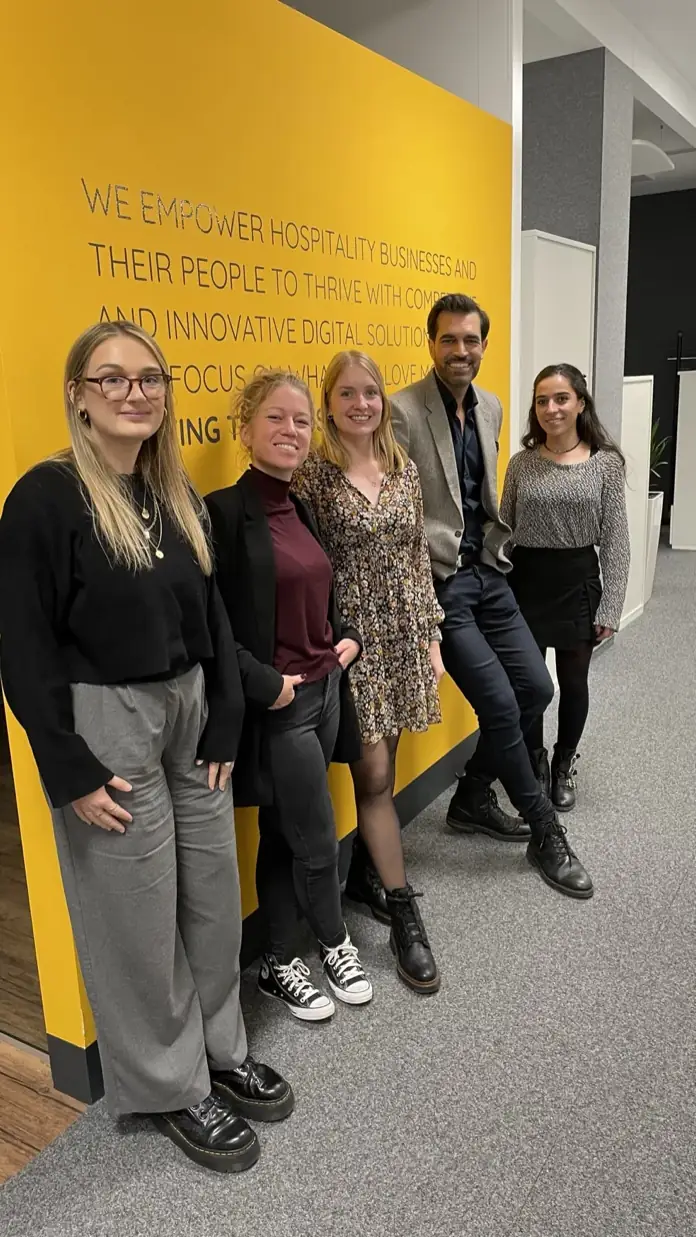 Alex Khan mit dem Team von DISH vor der gelben Wand mit dem Unternehmensleitsatz